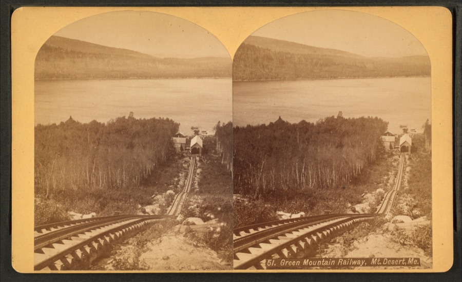 A stereoview of the Green Mountain Railway tracks descending through trees on Mount Desert Island, with Eagle Lake visible in the background.