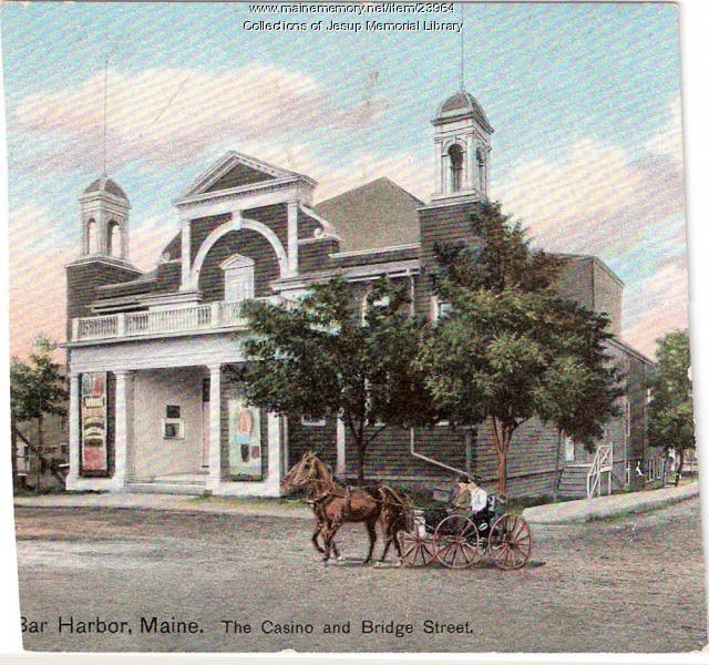 A colored postcard view of the Casino building on Bridge Street in Bar Harbor, a tall wooden hall with two cupolas, with a horse-drawn carriage in the foreground.