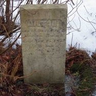 A weathered white marble gravestone, partly buried in snow, the inscription almost completely worn away.